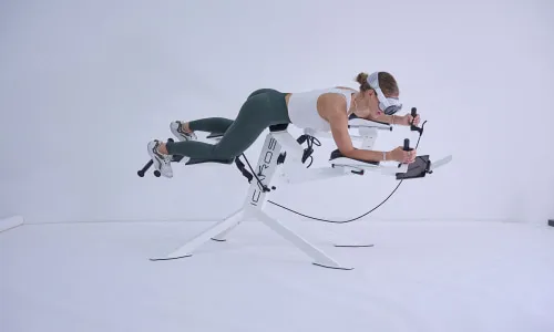 Frau trainiert auf dem futuristischen ICAROS®-Lightning-Gerät in weißem Raum – Virtual-Reality-gestütztes Bewegungssystem in den Move & Relax Bereichen der Pletzer Resorts.