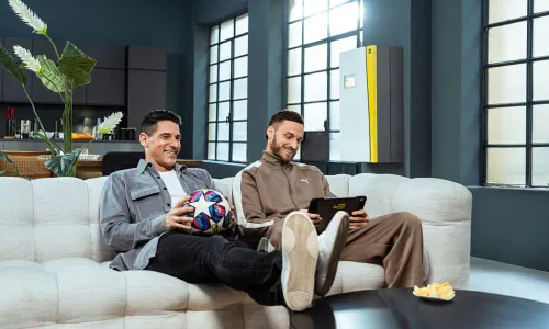Die Fußballstars Marko Arnautovic und Helge Payer entspannt auf einem Sofa, Teil der iDM-Werbekampagne für intelligente Wärmepumpen mit Humor und Starfaktor.